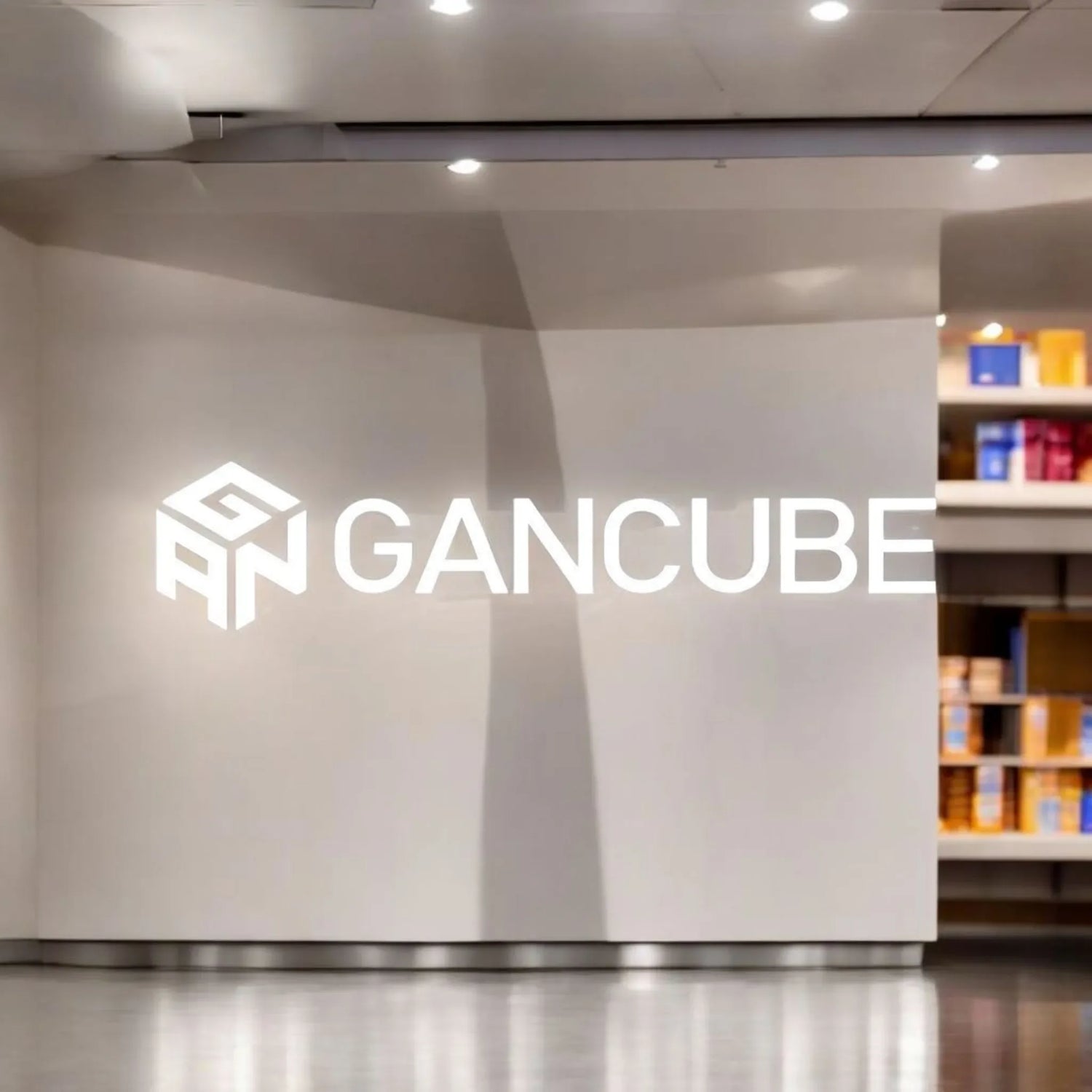 Logo de GANCUBE en pared blanca de tienda, cubos y accesorios de speedcubing al fondo